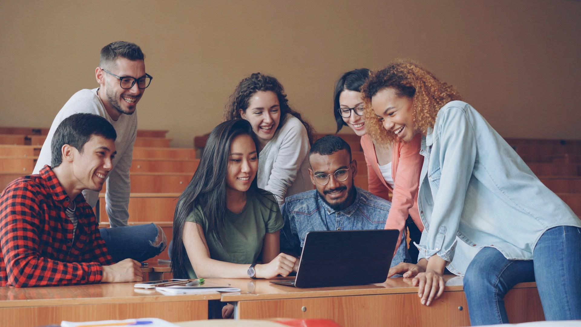 Group of people with different skin tones collaborating around a laptop